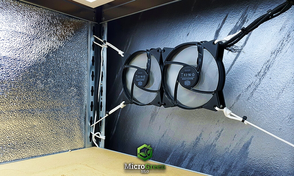 two electric fans running on a microgreen growing shelf